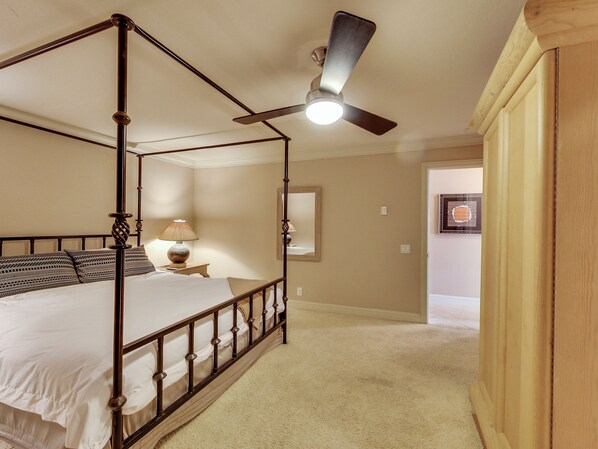 A four-poster bed with a ceiling fan, a bedside table with a lamp, and a framed picture on the wall.