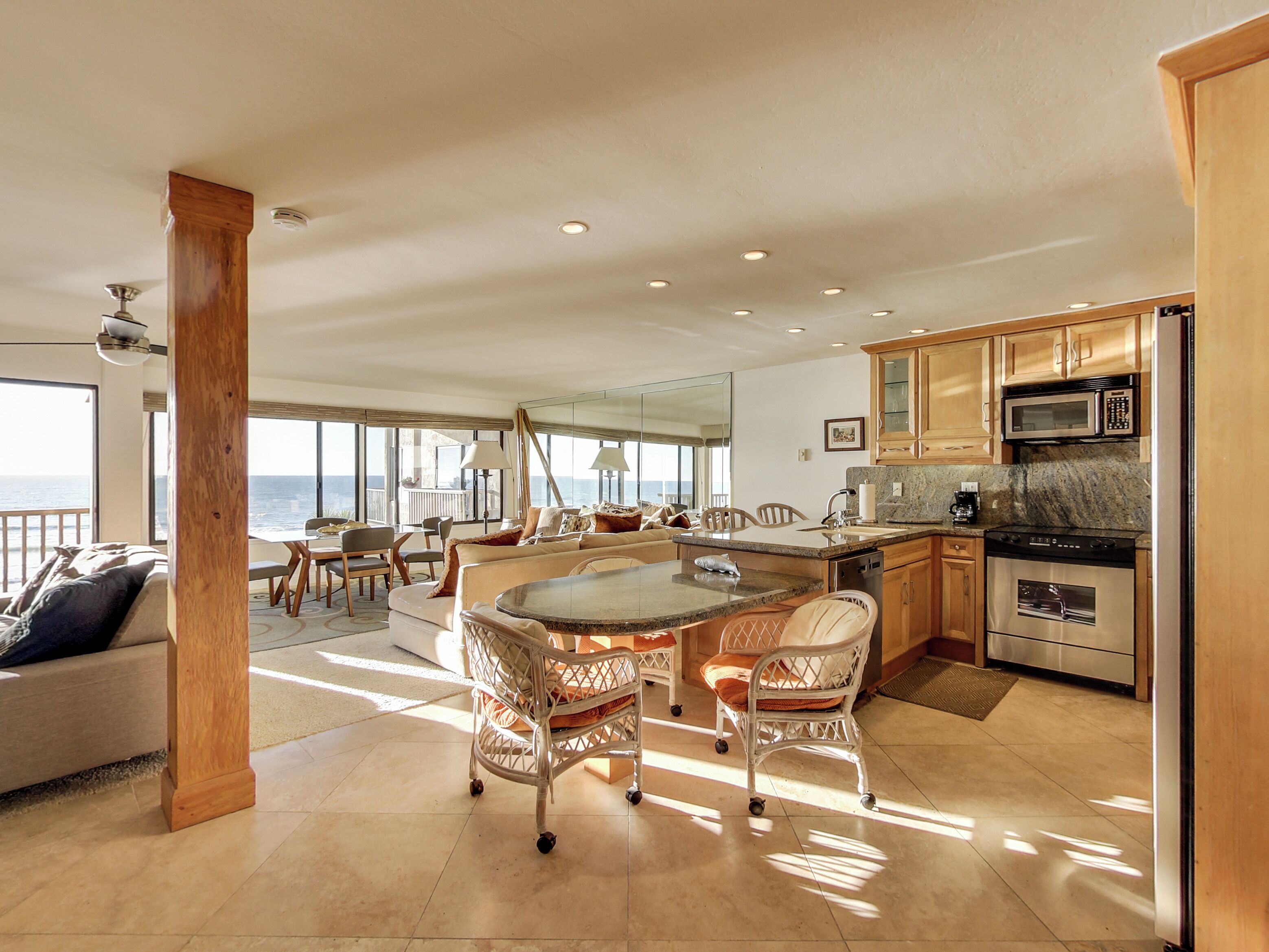 A spacious living area with a large island, dining table, and chairs, a kitchen with modern appliances, and a view of the ocean.