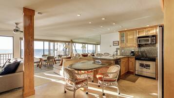 A spacious living area with a large island, dining table, and chairs, a kitchen with modern appliances, and a view of the ocean.
