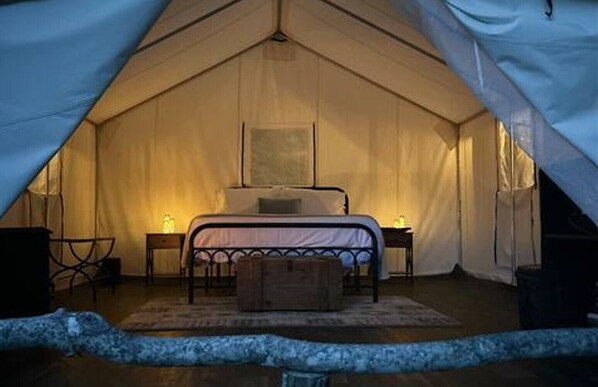 Une tente équipée d’un lit, de tables de chevet et d’un tapis.