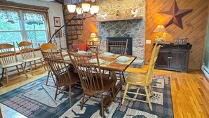Un coin repas avec une table et des chaises en bois, une cheminée et une décoration en forme d’étoile au mur.