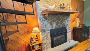 Un salon chaleureux avec une cheminée en pierre, un plancher en bois, une statue d’ours et un tapis à motifs.