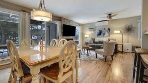 A spacious living room with a large TV, a dining area with wooden chairs, and a ceiling fan.