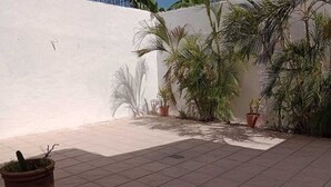 A courtyard with tiled flooring, potted plants, and a white wall.