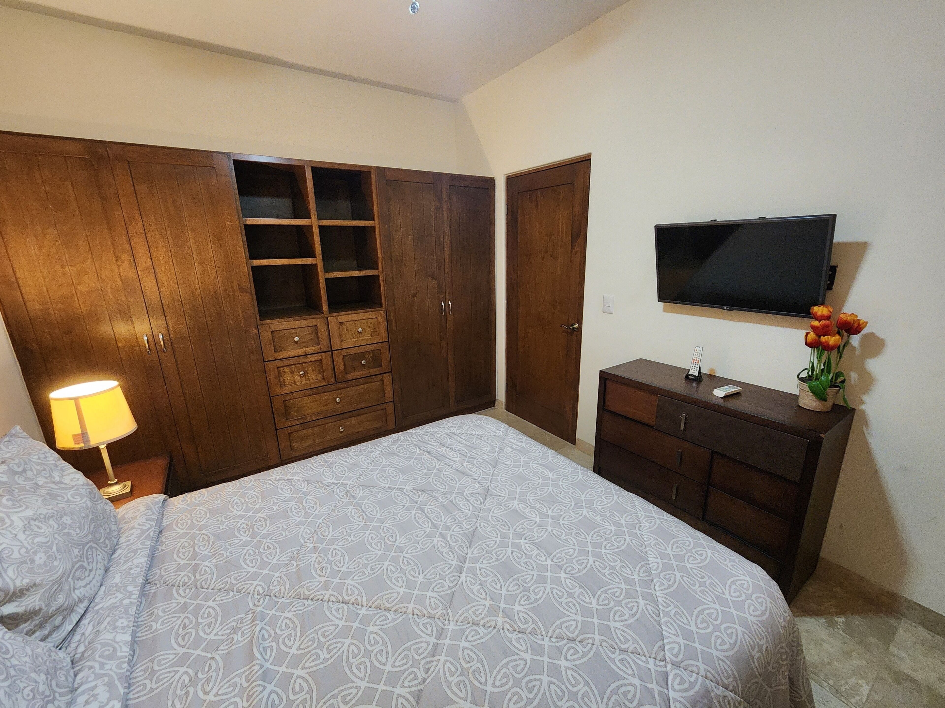 A bedroom with a bed, a wardrobe, a dresser, a TV, and a lamp.