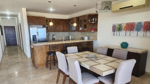 A modern kitchen with granite countertops, wooden cabinets, and a central island with bar stools. - Condo Ventanas  (Cabo San Lucas)