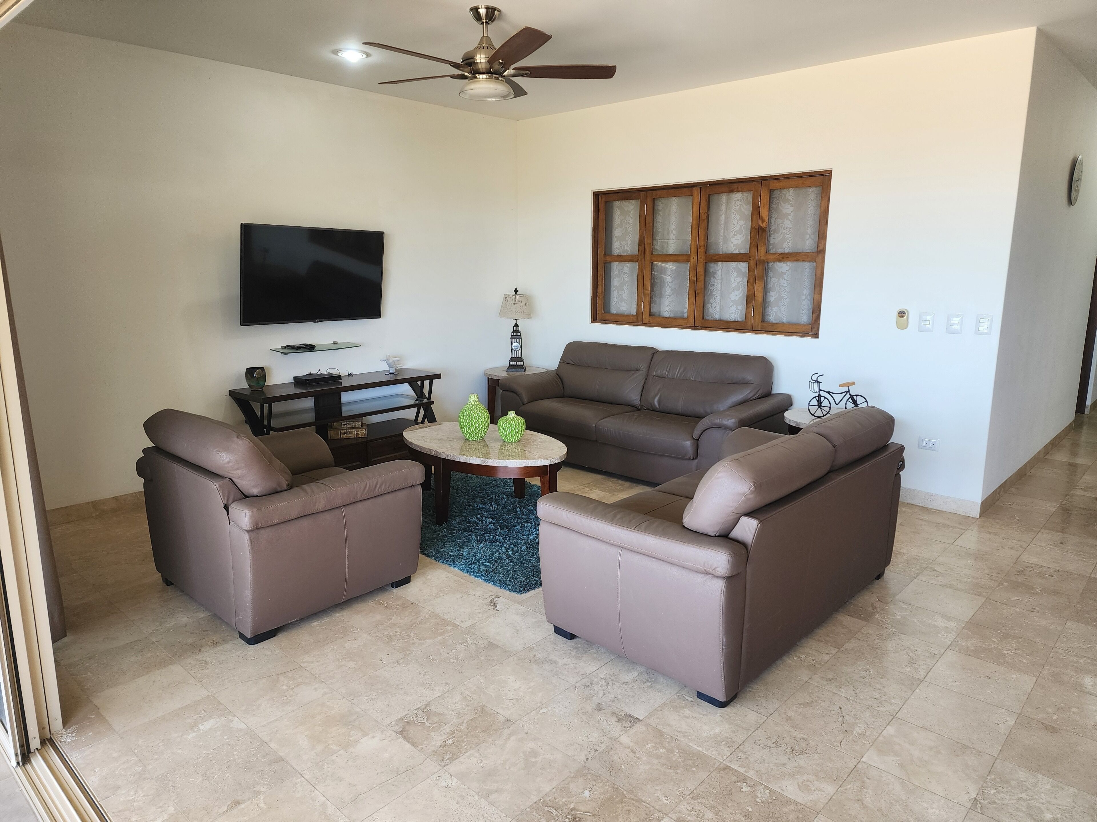 A living room with a ceiling fan, a flat-screen TV, a sofa set, and a coffee table.