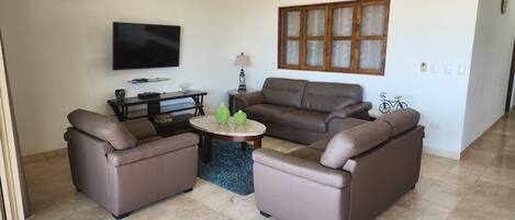 A living room with a ceiling fan, a flat-screen TV, a sofa set, and a coffee table.