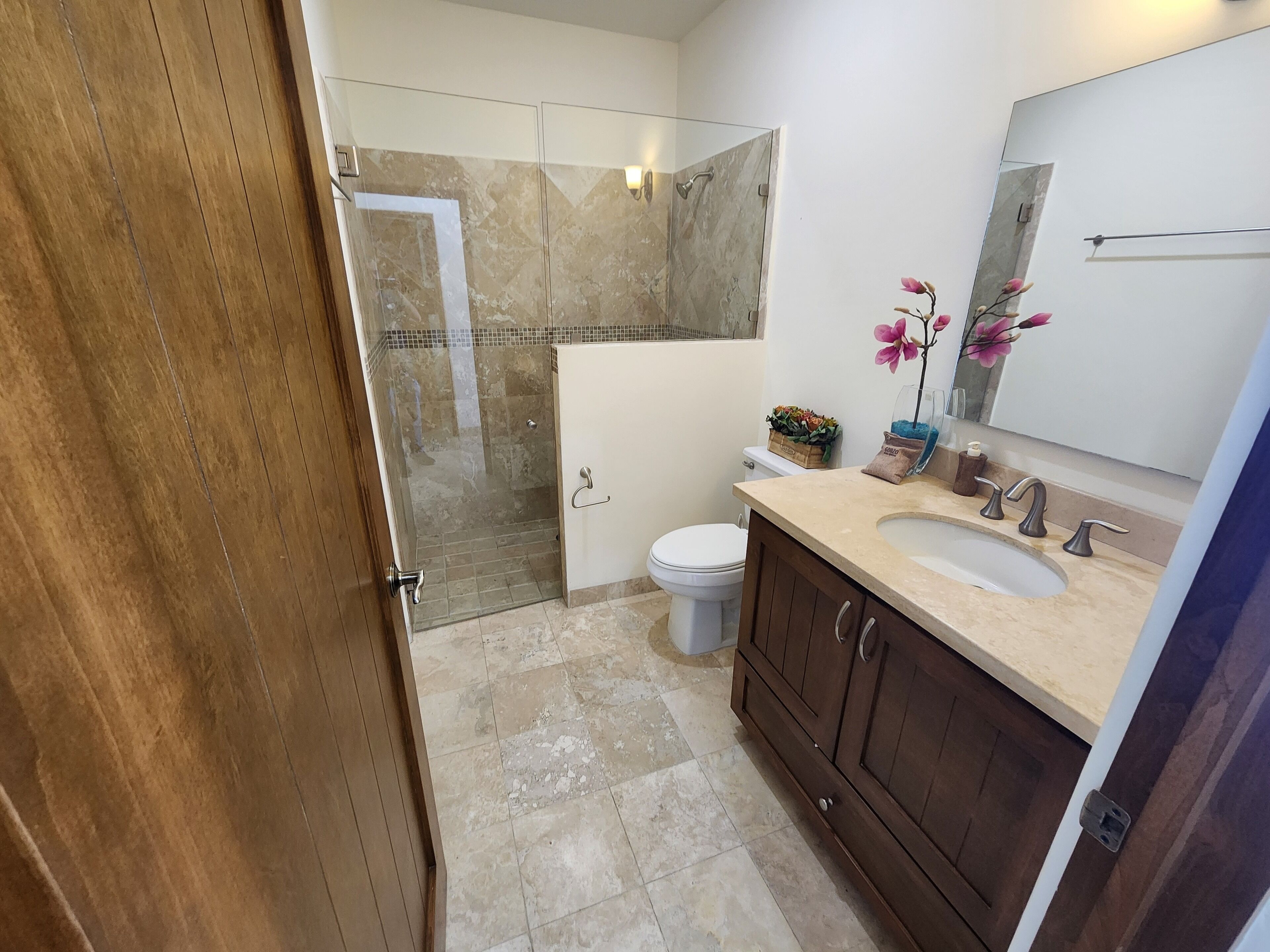 Un bany modern amb plat de dutxa de vidre, un vàter blanc, un lavabo beix i un moble de bany de fusta.