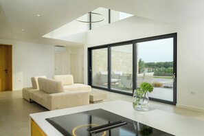 Uma sala de estar moderna com um sofá, uma mesa de jantar e vista para um pátio exterior através de grandes portas de correr.