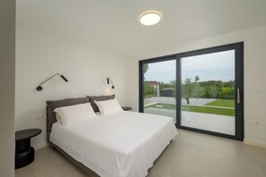 A bedroom with a large bed, two bedside tables, a ceiling light, and a view of a garden through a sliding door.