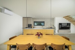 Uma cozinha moderna com uma ilha central, uma mesa de jantar com cadeiras e uma TV fixada na parede.