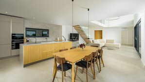 A modern kitchen with a central island, a dining area with a wooden table and chairs, and a staircase leading to an upper level.