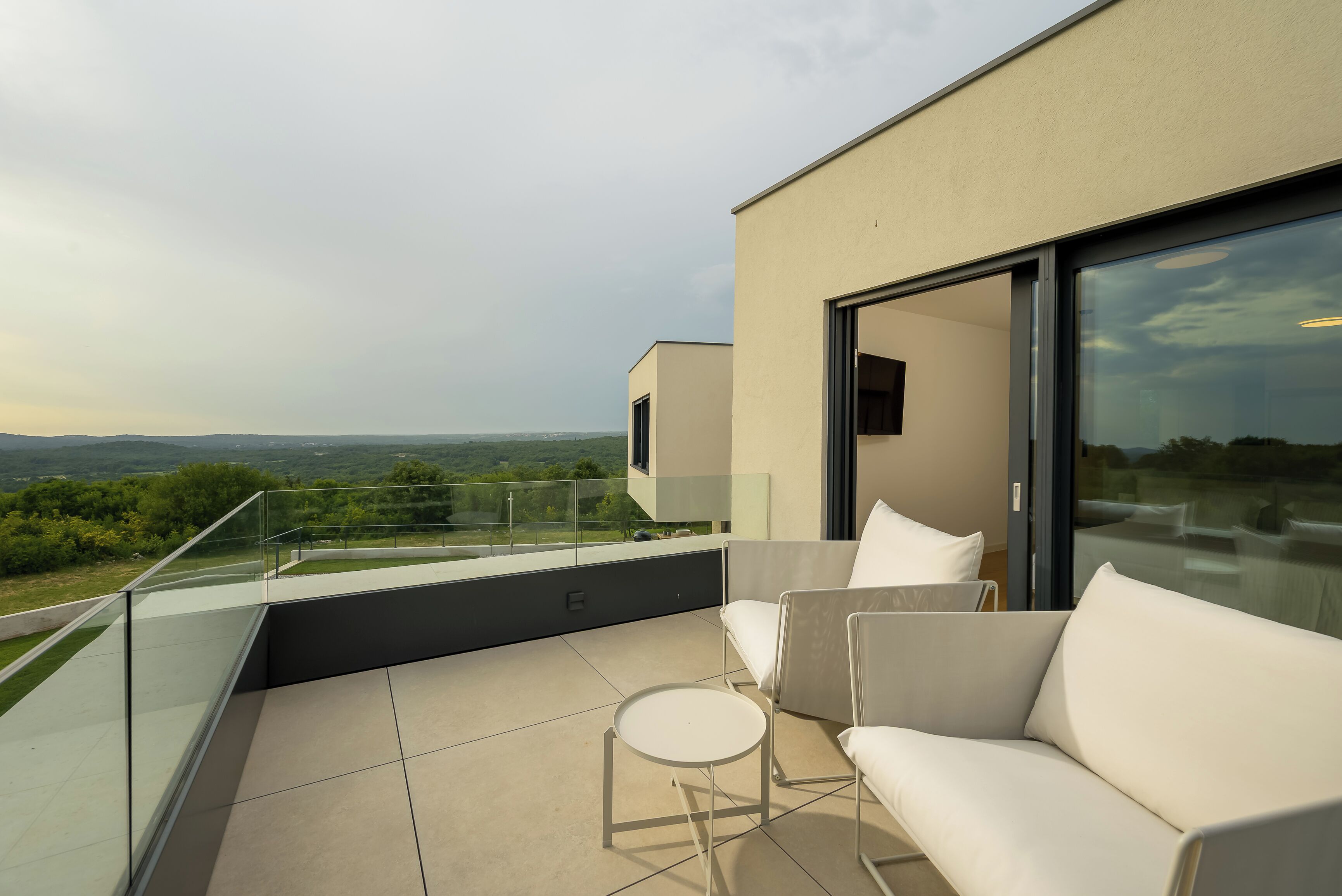 Un balcón moderno al aire libre con sofá y una pequeña mesa, con vistas al paisaje.