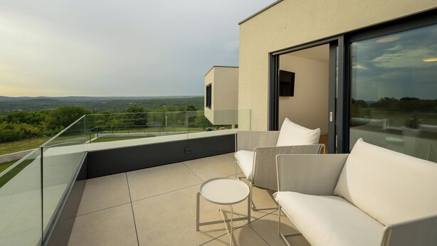 A modern outdoor balcony with a sofa and a small table, offering a view of the landscape.