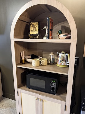 Uma estante de madeira com micro-ondas, objetos decorativos e livros.