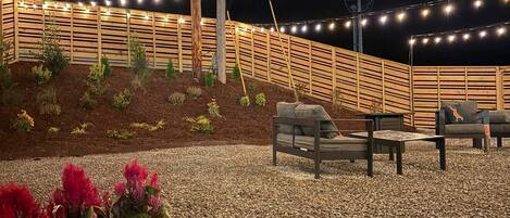 A patio area with a wooden fence, string lights, and outdoor seating.