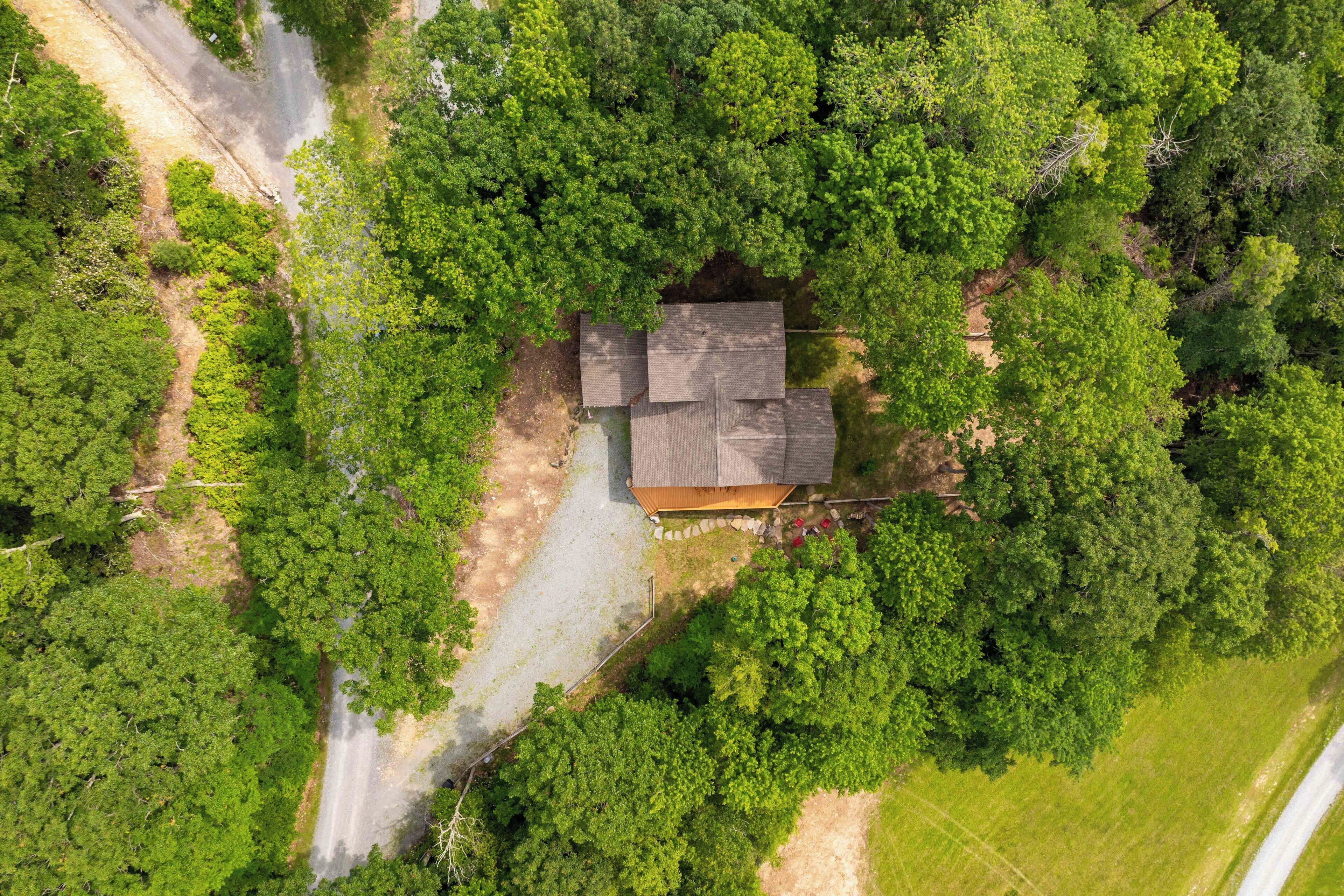 Une vue aérienne d’une maison entourée d’arbres verdoyants et touffus, avec une allée bien visible et un petit jardin.
