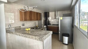 A modern kitchen with a central island, wooden cabinets, and a view of the city through large windows. - 3 bedroom family apartment in Acapulco, a few steps from the beach. (Acapulco de Juárez)