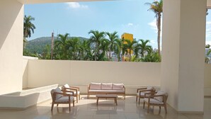A spacious balcony with a sofa, chairs, and a tiled floor, overlooking a cityscape with palm trees and a mountain. - 3 bedroom family apartment in Acapulco, a few steps from the beach. (Acapulco de Juárez)