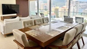 A modern living room with a large wooden dining table, beige sofas, and a flat-screen TV. - 3 bedroom family apartment in Acapulco, a few steps from the beach. (Acapulco de Juárez)