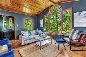 A spacious living room with a large window, a sofa set, a coffee table, and a leather armchair.