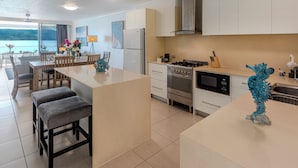 A modern kitchen with a central island, a dining area with chairs and a table, and a view of the outdoors.