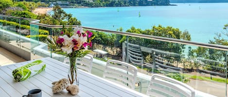 A balcony with a table set for two, overlooking a scenic coastal view.