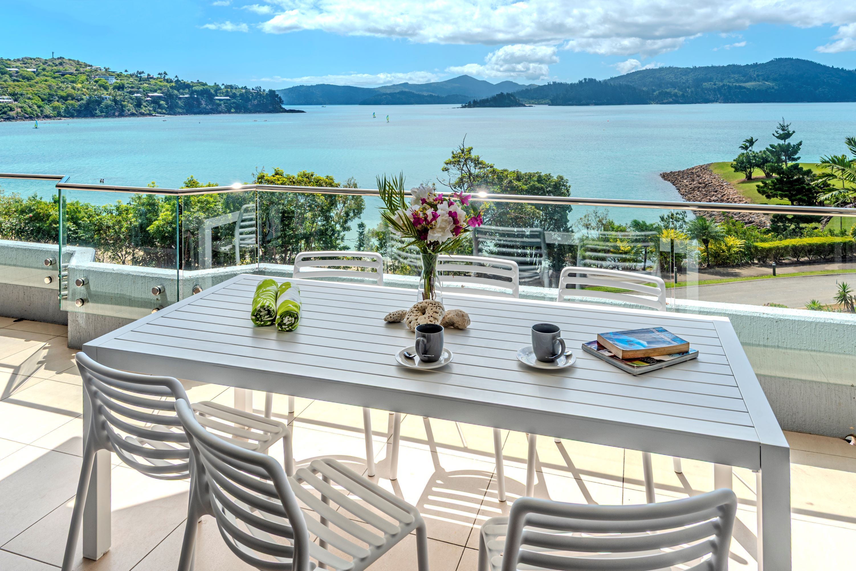 A balcony with a table, chairs, and a vase of flowers.