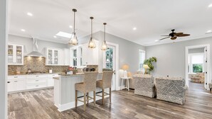 Una cocina amplia con armarios blancos, una isla central con taburetes y una zona de comedor con un sofá estampado.