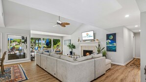 A modern living room with a large sectional sofa, a fireplace, and a television mounted on the wall. - 22 Heath Drive @ Palmetto Dunes | Private Pool | Golf Course View (Hilton Head Island)
