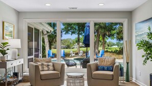 A living room with a sofa, two armchairs, a coffee table, and a view of a backyard with a pool and patio furniture. - 22 Heath Drive @ Palmetto Dunes | Private Pool | Golf Course View (Hilton Head Island)
