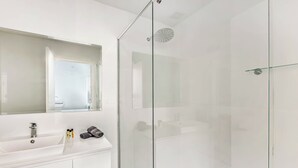 Een moderne badkamer met een douchecabine van glas, een witte wastafel met een spiegel erboven en toiletartikelen op het aanrecht.