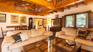 A cozy living room with a wooden ceiling, a large sofa set, a coffee table, and a dining area with chairs. - Villa El Ñeru - Bufones de Pría, Llanes (Belmonte De Pria)