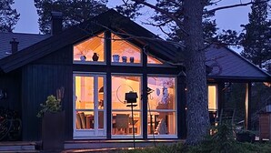 Une maison moderne avec de grandes fenêtres en verre, un porche et un arbre devant.