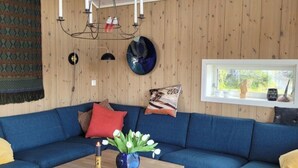 Un salon chaleureux avec un canapé bleu, un mur en bois, un lustre et une fenêtre donnant sur un beau paysage.