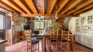 A rustic kitchen with wooden beams, stone walls, and a dining area with wooden chairs and a table. - Llanes House with Garden - La Casa del Güelu (Hontoria)