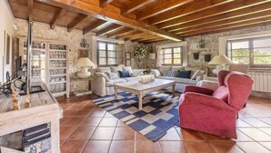 A rustic living room with exposed wooden beams, a checkered rug, and a mix of white and pink furniture. - Llanes House with Garden - La Casa del Güelu (Hontoria)