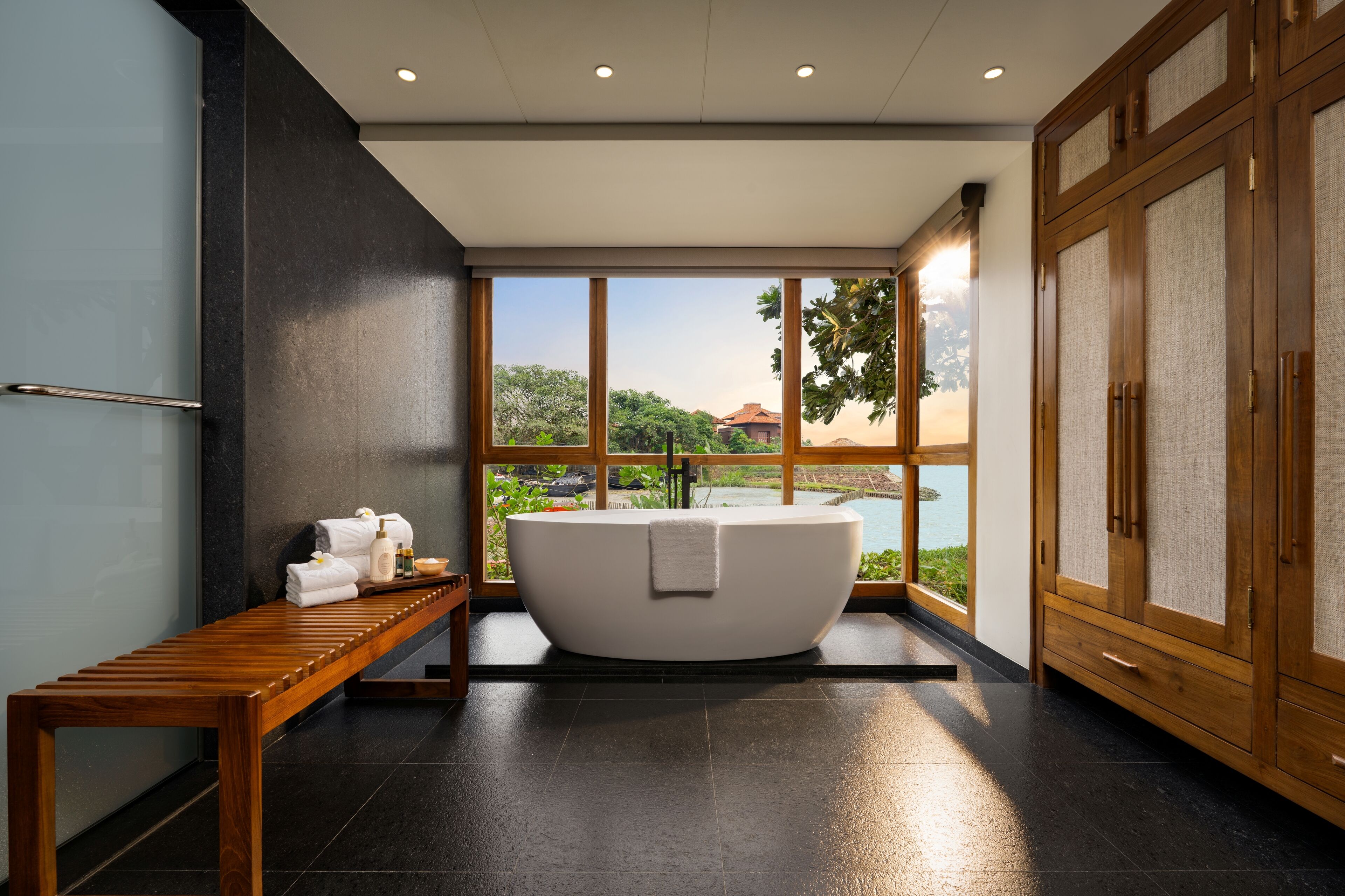 Ein modernes Badezimmer mit einer freistehenden Badewanne, einer hölzernen Sitzbank und Blick ins Freie.