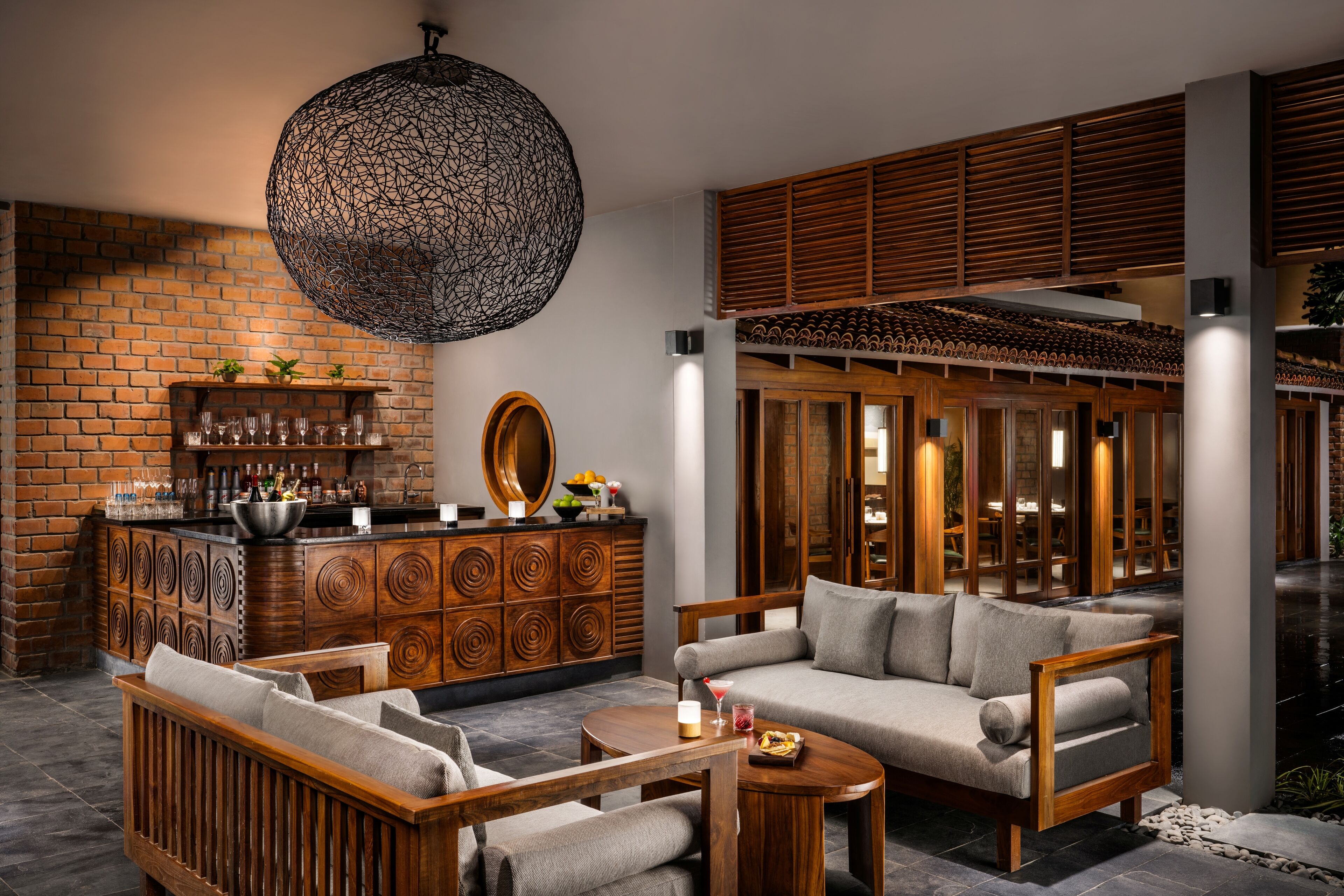 A modern bar area with a brick wall, wooden furniture, and a large hanging light fixture.