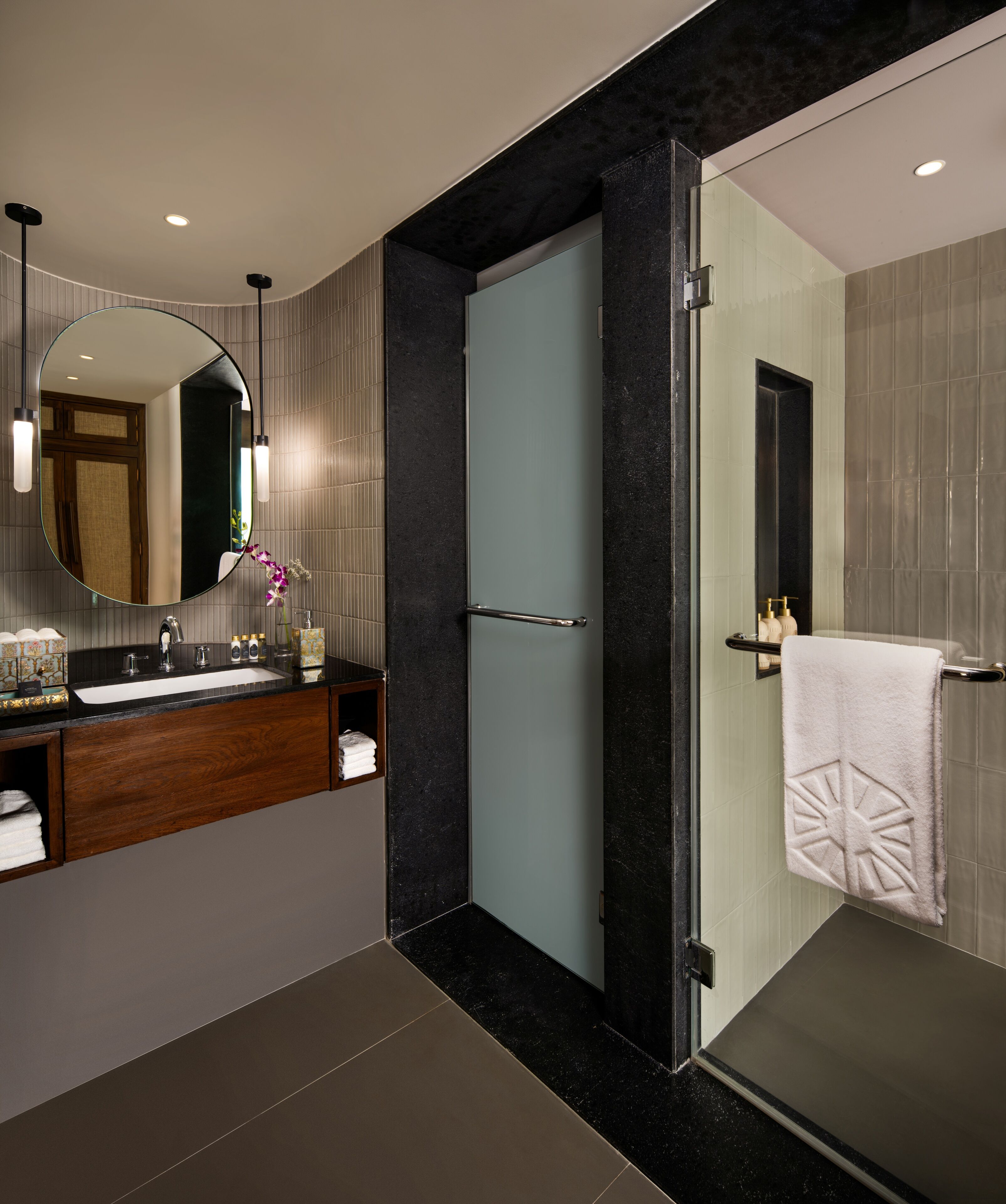 A modern bathroom with a large mirror, dark marble countertops, a glass shower enclosure, and a towel rack with a decorative towel.