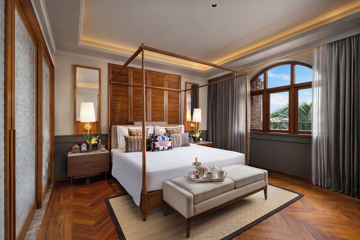 Um quarto espaçoso com cama de dossel, mesa de cabeceira com abajur e vista para o exterior por uma grande janela.