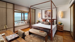 Un dormitorio amplio con una cama grande, vistas al mar, un escritorio de madera y un banco.