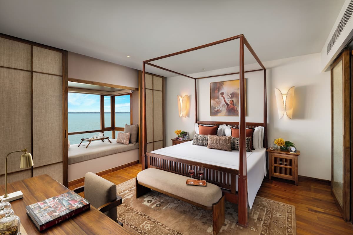 Quarto espaçoso com cama grande, vista para o mar, escrivaninha de madeira e um banco.