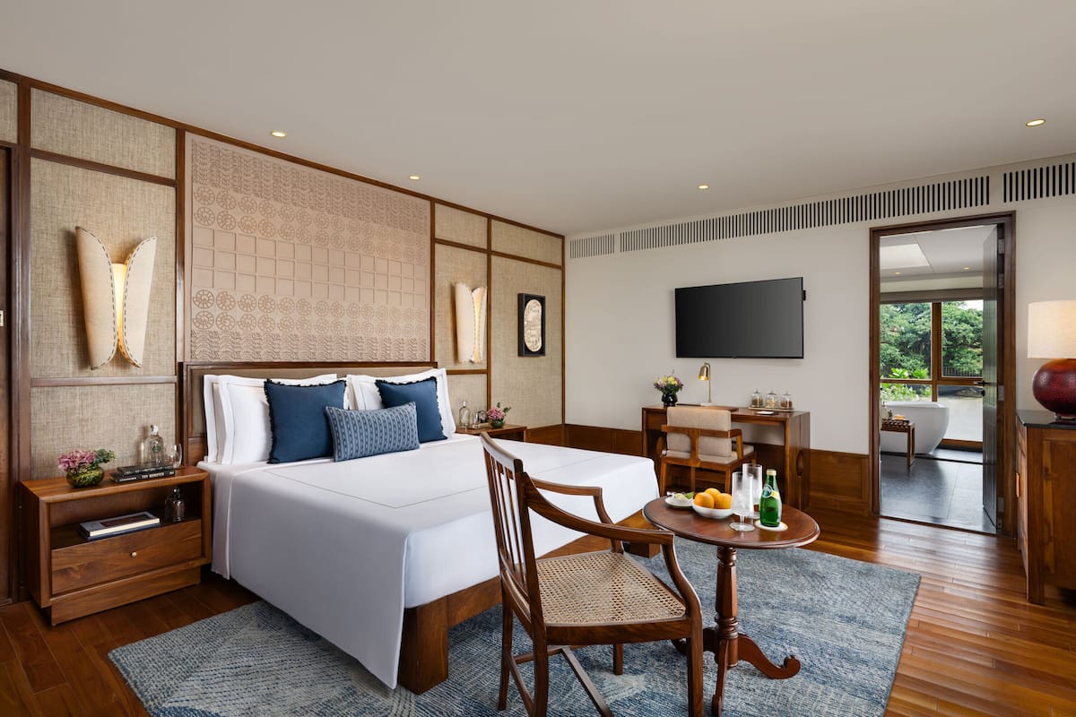 Quarto de hotel com uma cama grande, uma escrivaninha, uma cadeira, uma televisão e vista para o exterior.