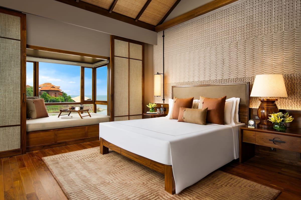 Quarto de hotel moderno com cama grande, vigas de madeira, vista para o mar e um painel tecido tradicional.