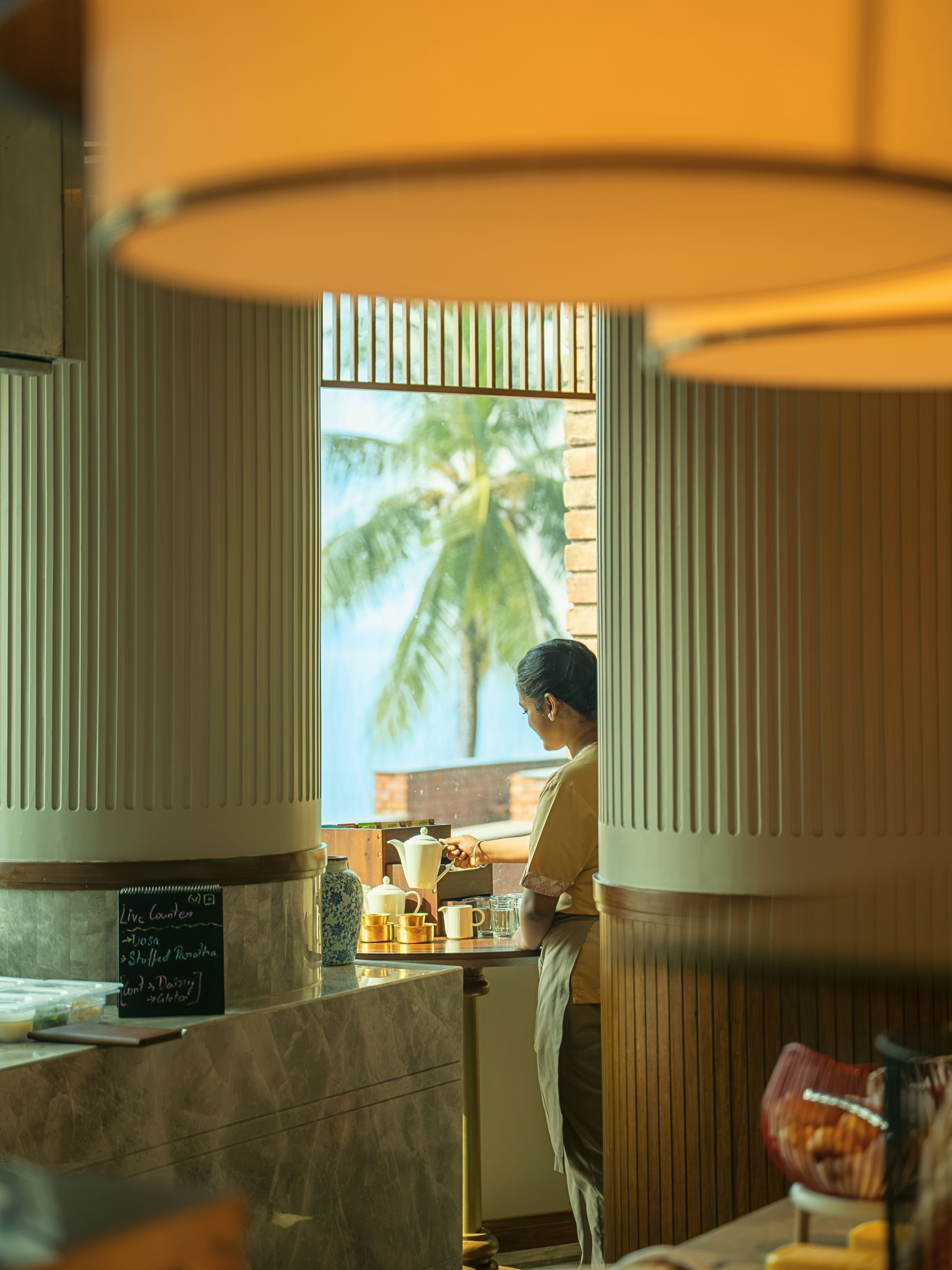 A person preparing a drink at a counter with a view of palm trees outside.