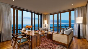 Una habitación con una mesa de comedor de madera, sillas, un sofá y vistas al mar a través de amplios ventanales.