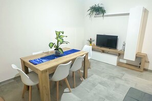 Ein Essbereich mit einem Holztisch, weißen Stühlen, einer blauen Tischmatte und einem Blumentopf.