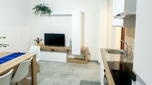 A compact kitchen with a built-in TV, a dining area with a table and chairs, and a small plant. - aMare Apartment, cozy accommodation a few steps from the sea (Nettuno)